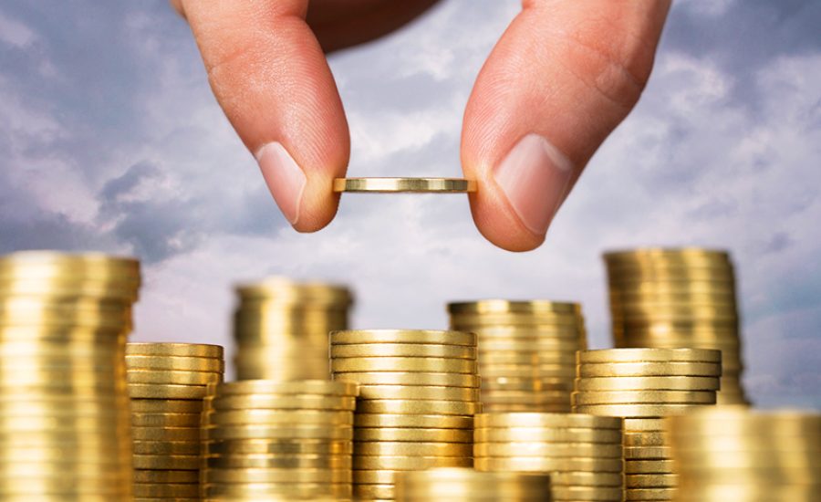 Savings, close up of male hand stacking golden coins over sky ba