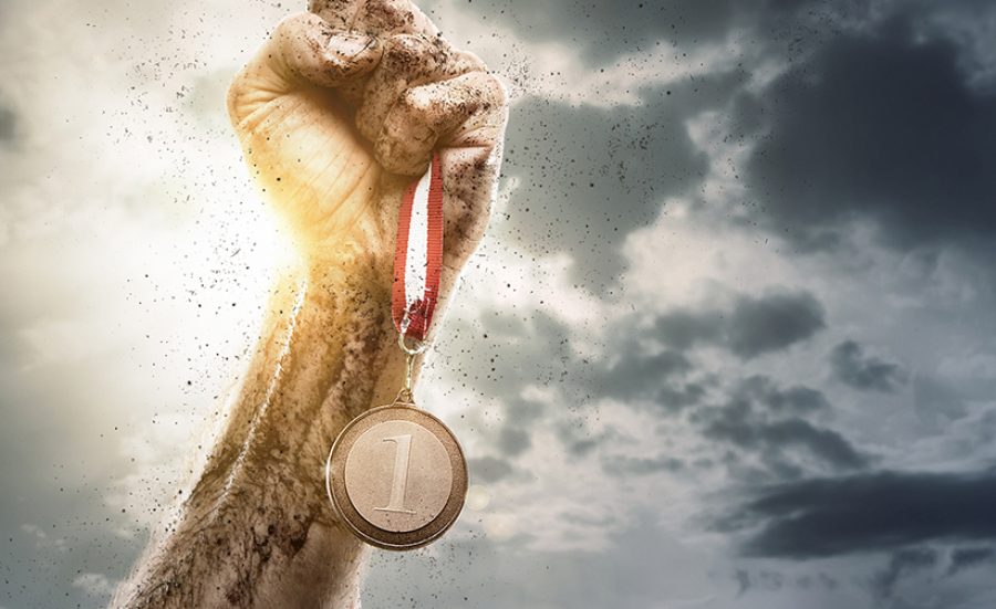 Success, male hand holding gold medal against the dramatic sky