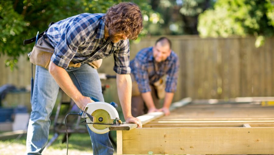 Carpenter Cutting Wood With Handheld Saw While Coworker Helping