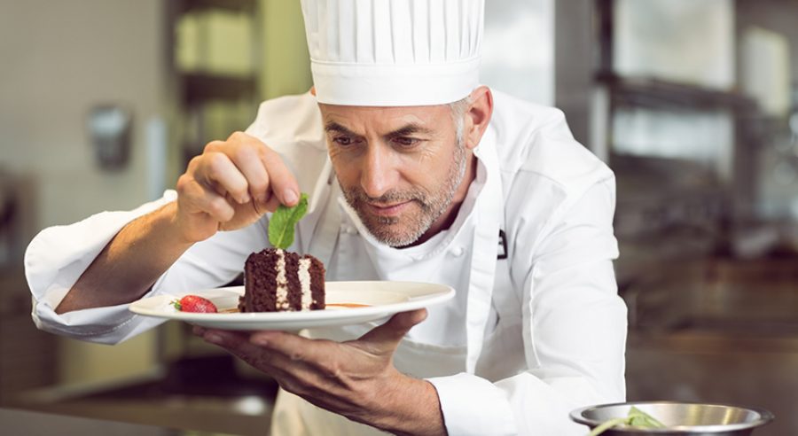 Closeup of a concentrated male pastry chef decorating dessert in the kitchen