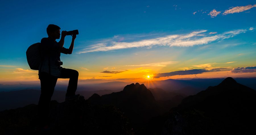 Photographer man on mountain reaches for the sun