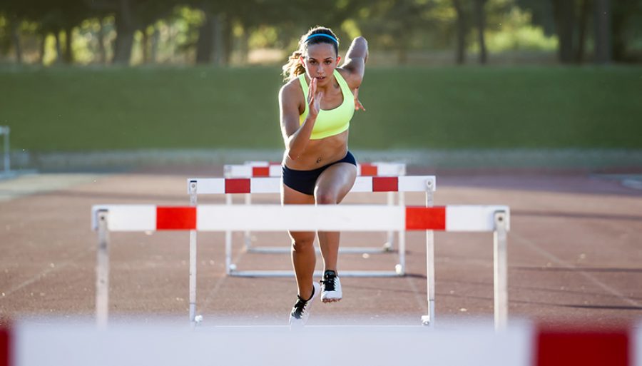 Young athlete jumping over a hurdle during training on race trac