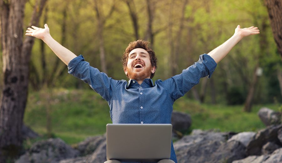 Happy hipster with laptop in the forest